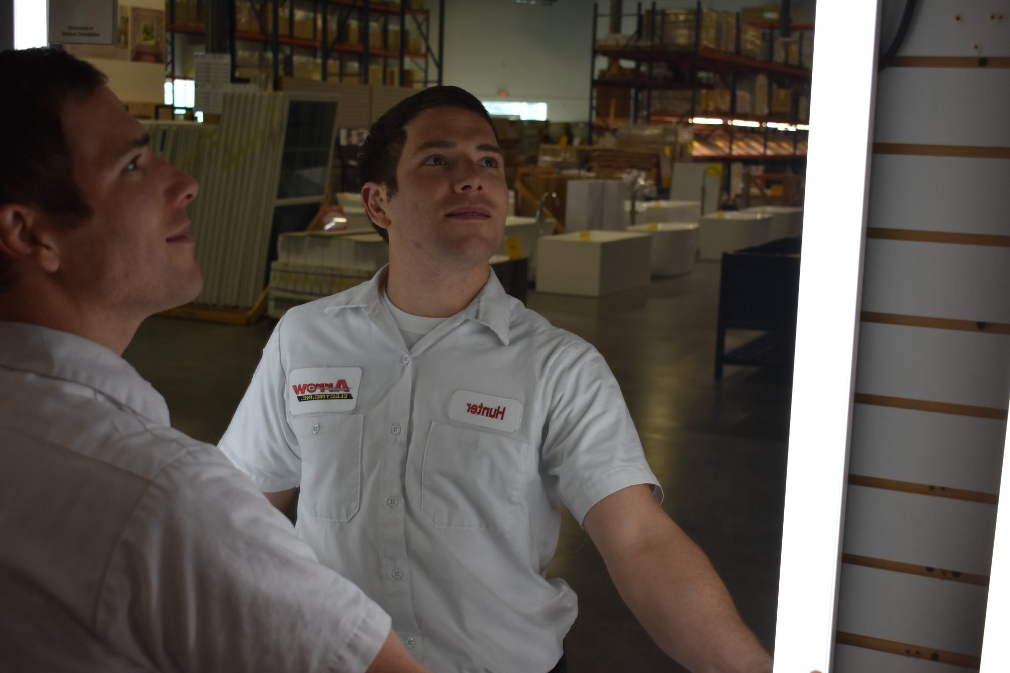 Arrow Electric employees evaluating a lighting fixture in a warehouse.