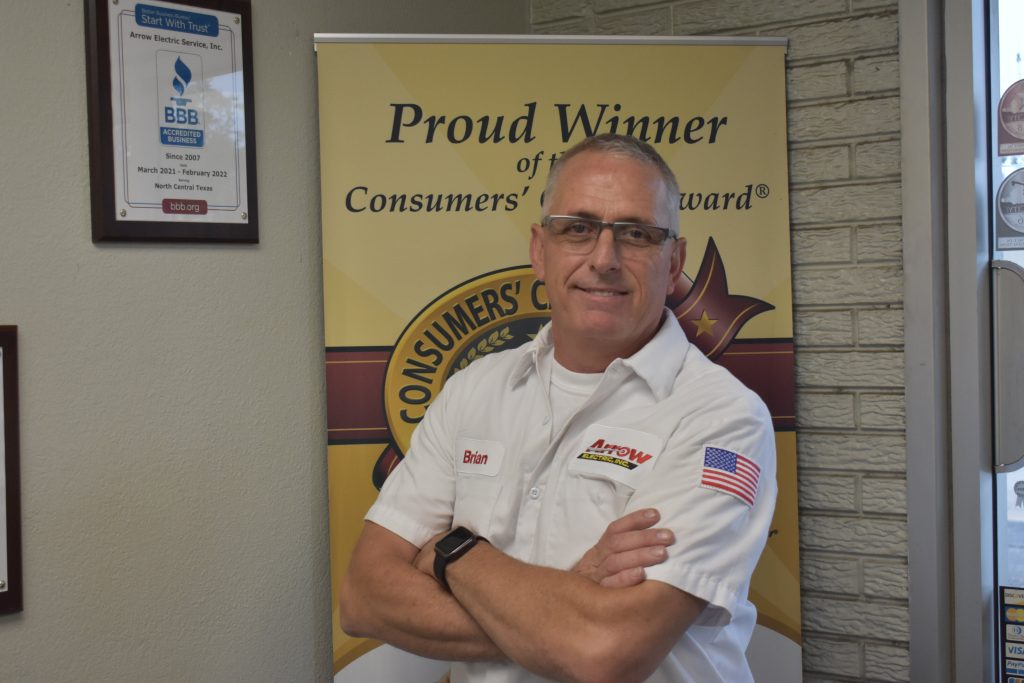 Commercial manager of Arrow Electric standing with arms crossed in front of the company's award banners.